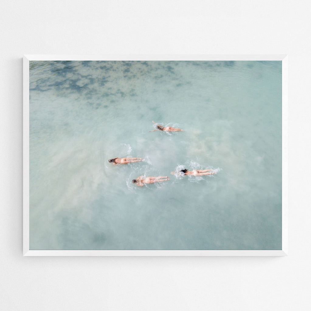 An aerial photograph captures four women swimming nude in the tropical waters of Sayulita, Mexico. The sun-kissed babes exude confidence and freedom, buns outs, as they enjoy a carefree moment in the chalky blue water.
